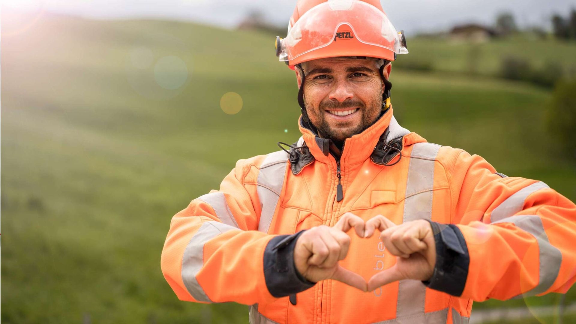 Ein Mitarbeiter von cablex in einer grünen Landschaft, der mit seinen Händen ein Herz formt.